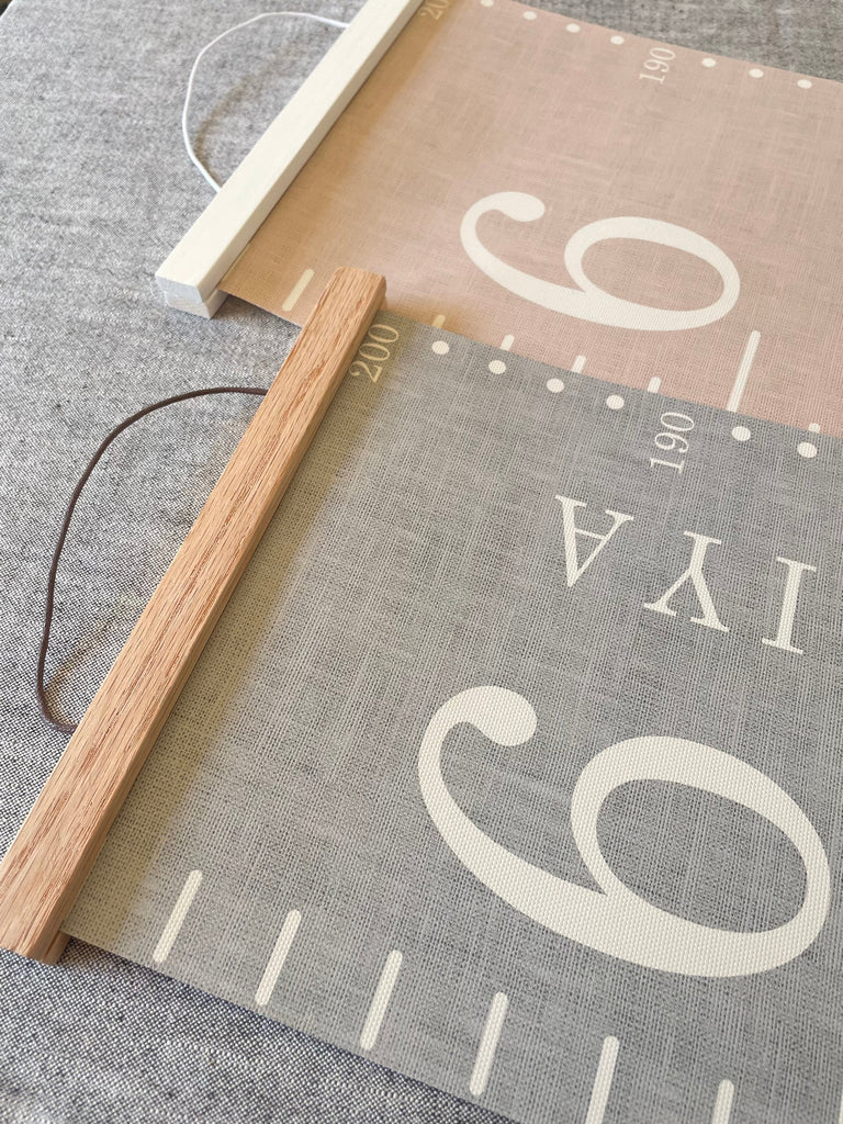 Two textured canvas fabric height charts with printed numbers and  wooden hangers one in oak and the other in white.