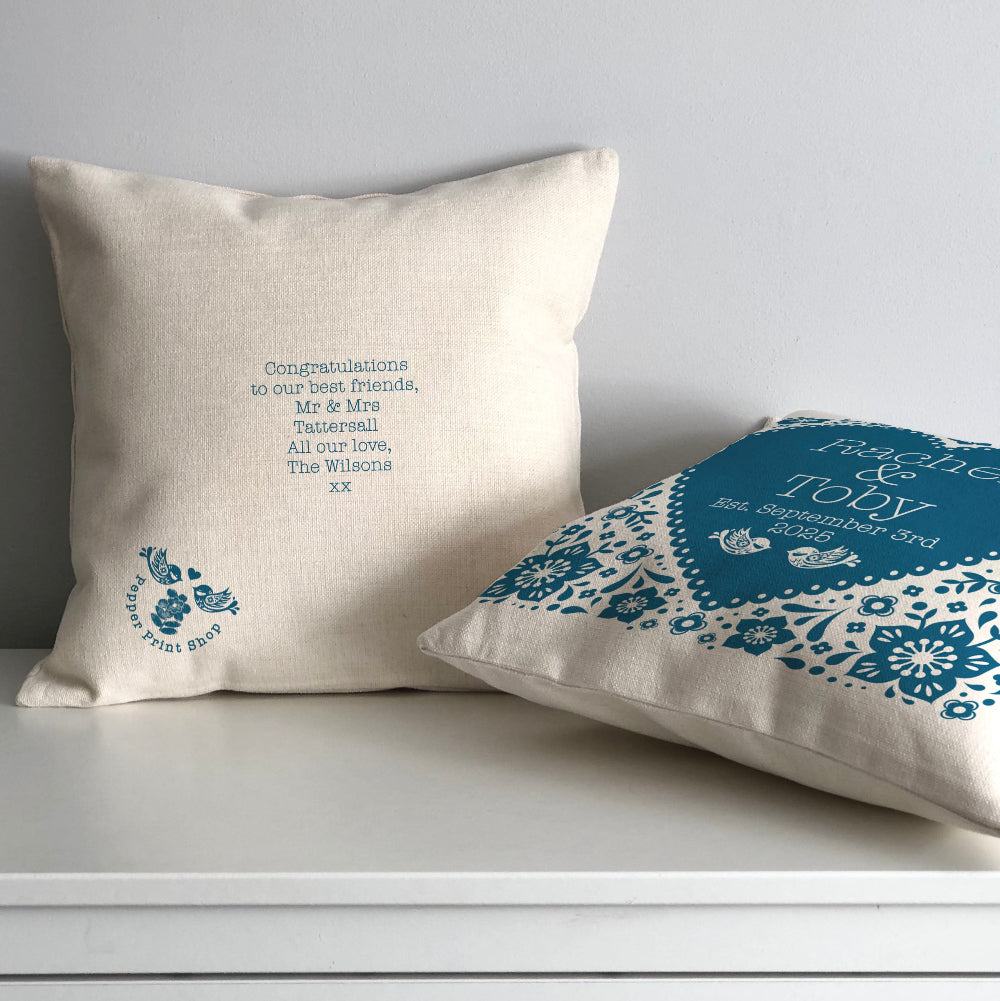 Two examples of decorative cushions one showing a personal message which will be presented on the back and the other with a floral heart pattern on the front show the names of the new married couple. 